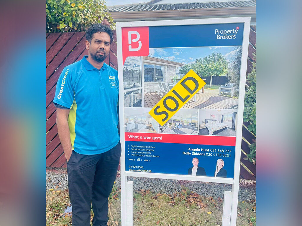 Cleaner standing by real estate sold sign.