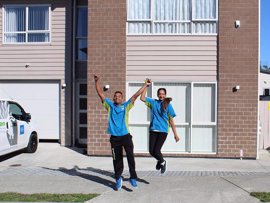 Cleaners jumping in the air outside their new home.