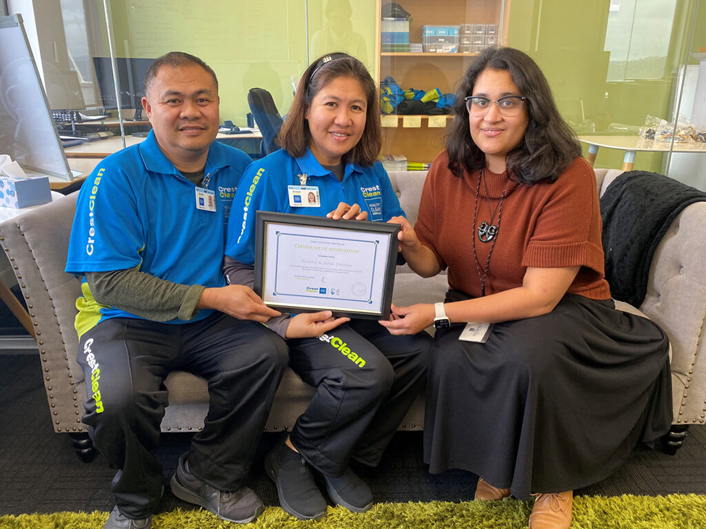 Cleaners sitting on sofa holding certificate.